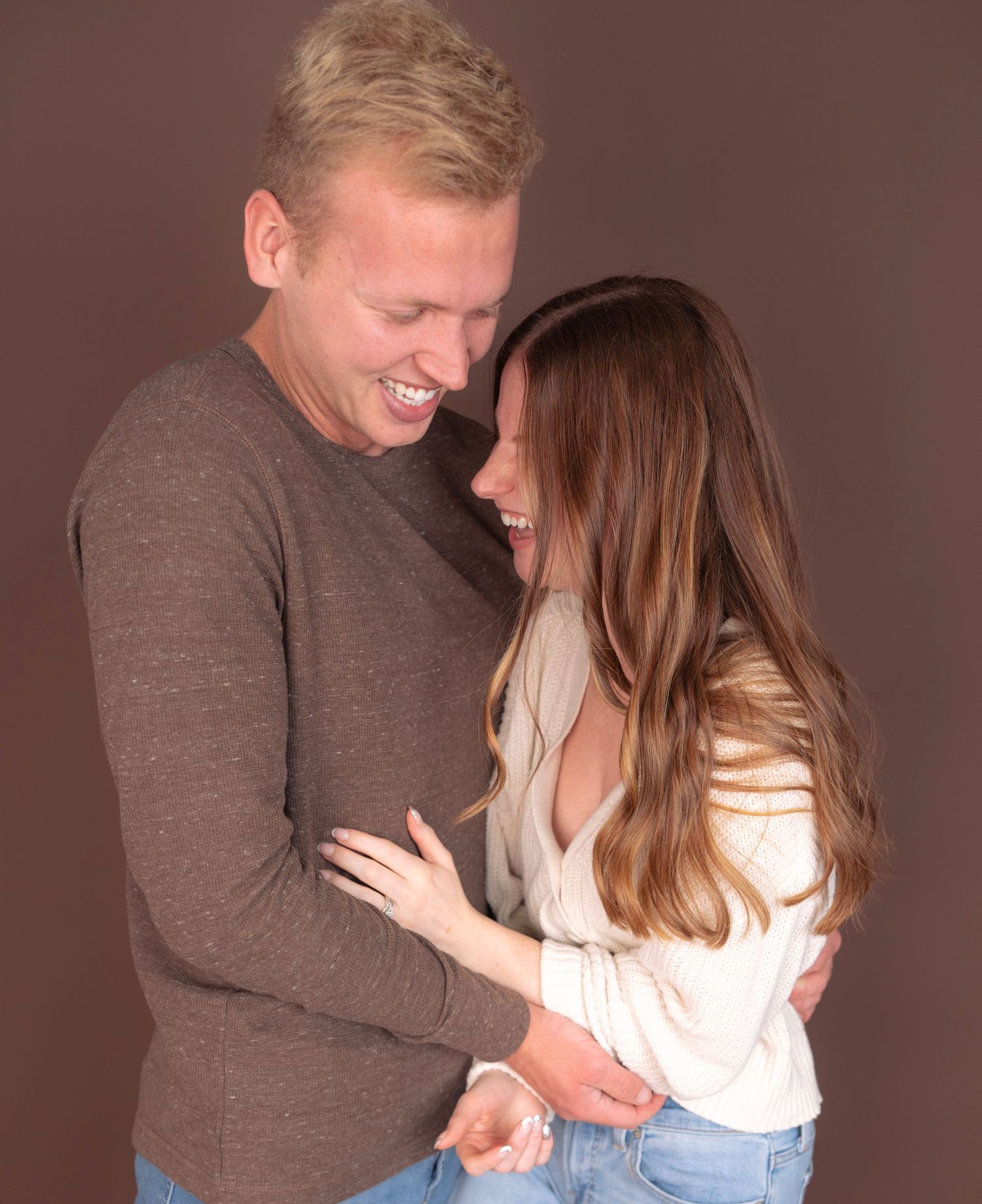 A tender moment between a couple in casual attire against a brown background.