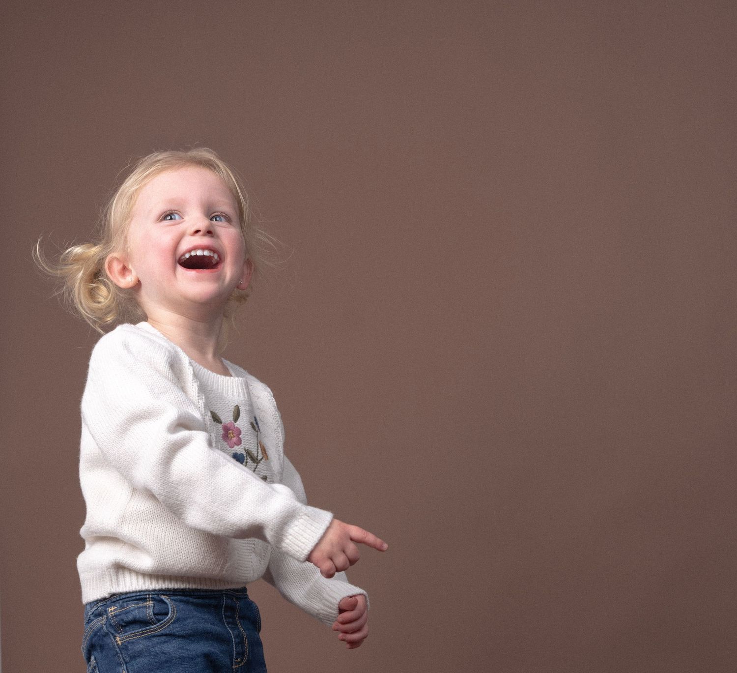 Energetic poses in cream sweater and jeans against brown background.