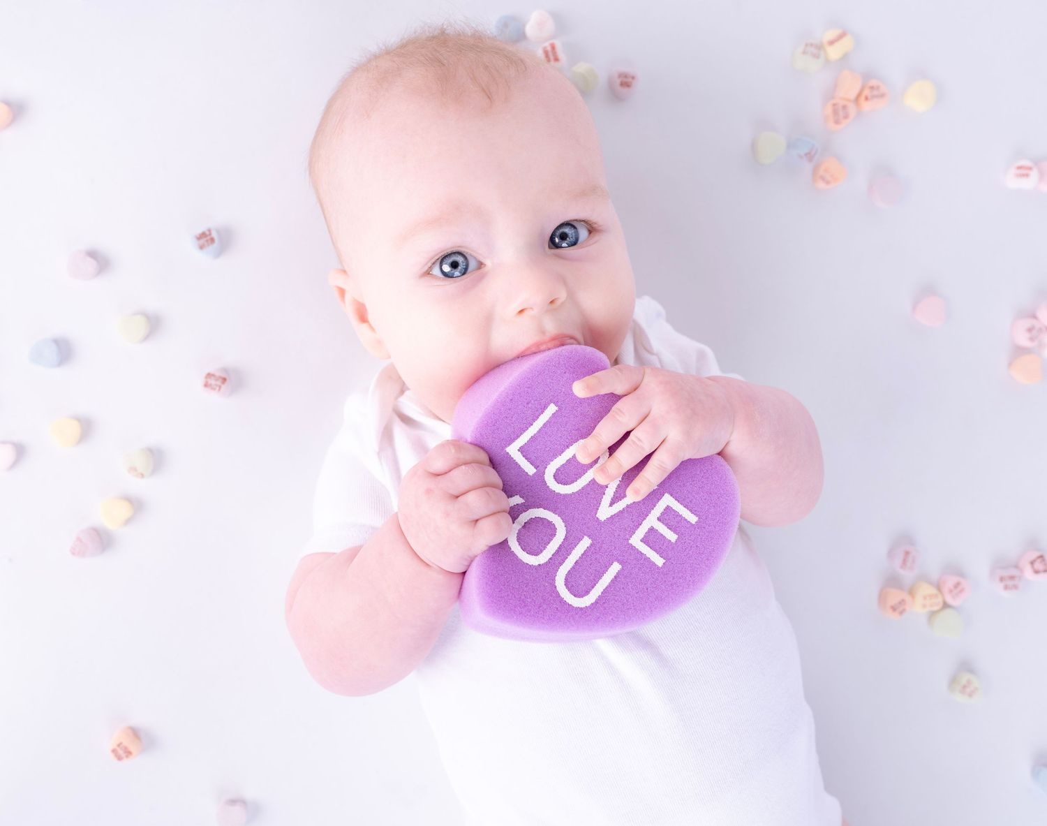Baby with purple heart-shaped Valentine's prop against light background.