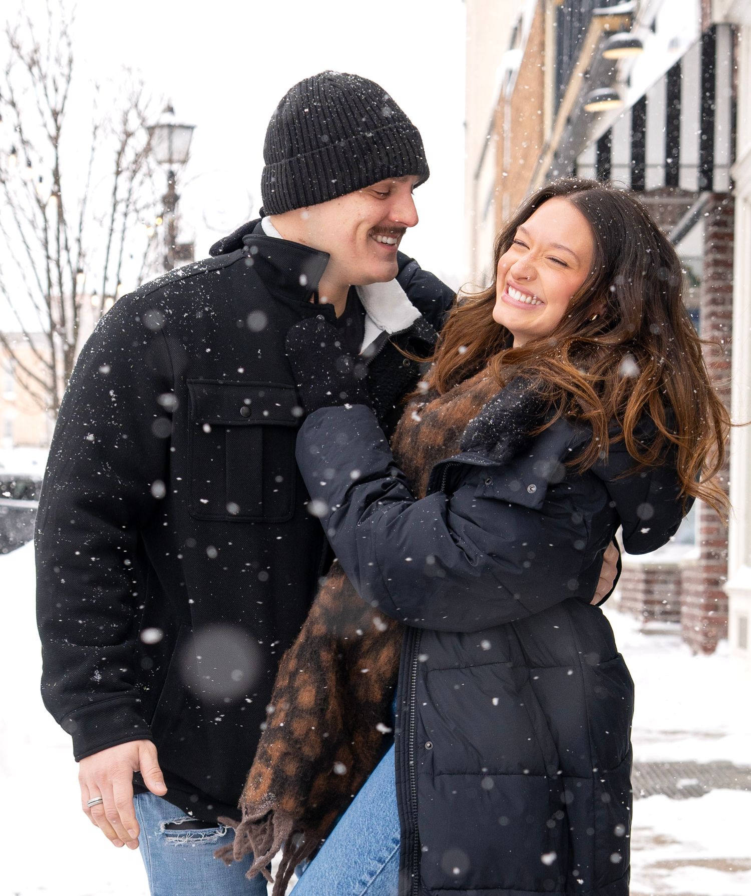 A joyful winter moment between a couple laughing together as snow falls around them.