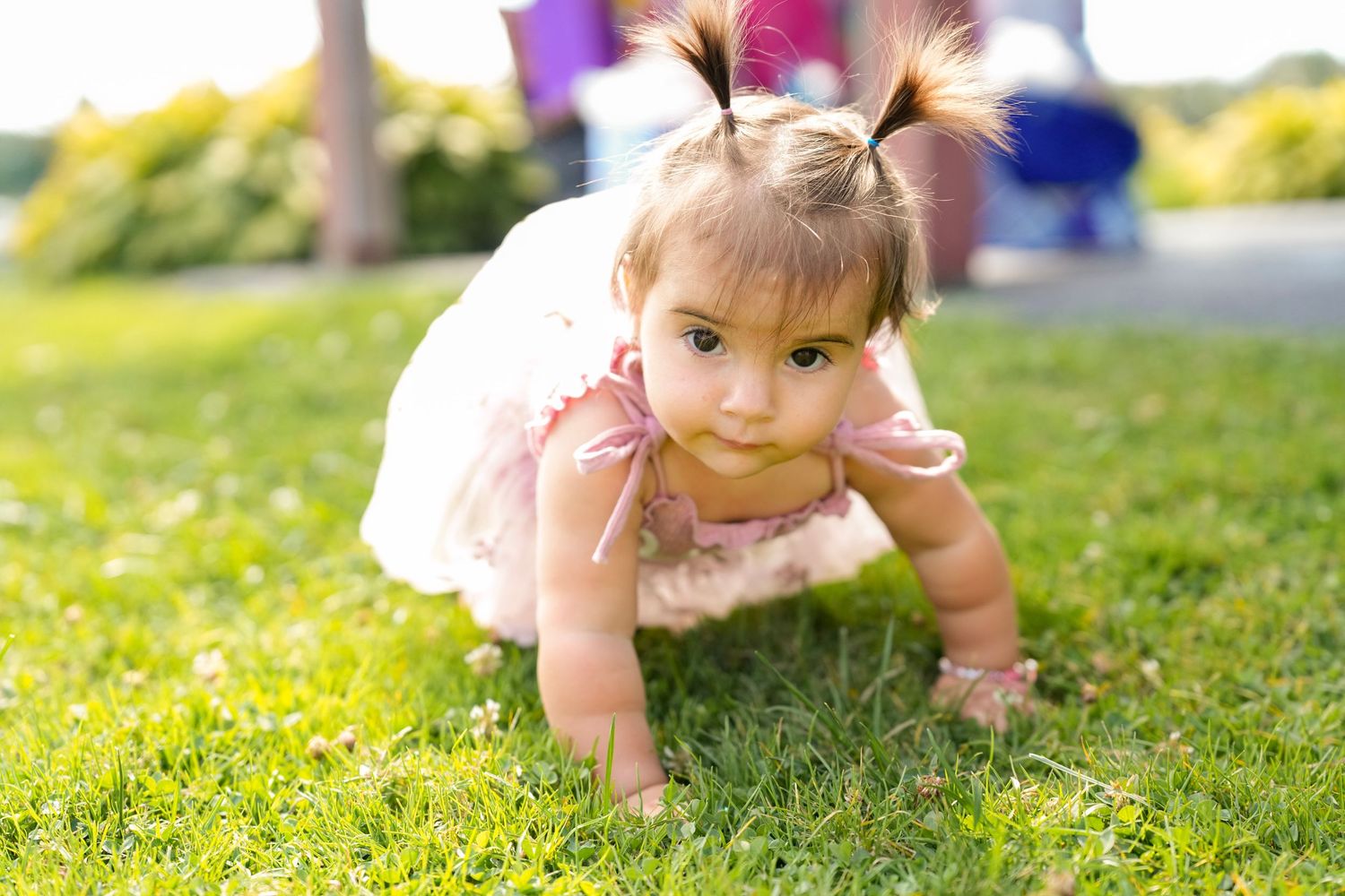 Child crawling on green grass wearing pink summer dress.