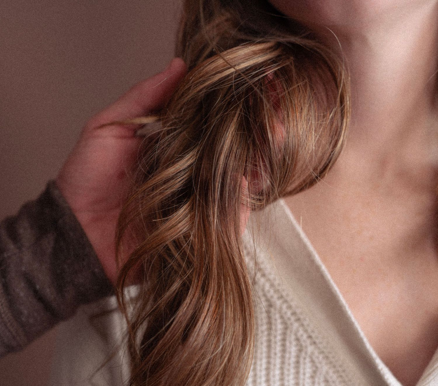 Close-up detail of long wavy brown hair and a cream-colored sweater.