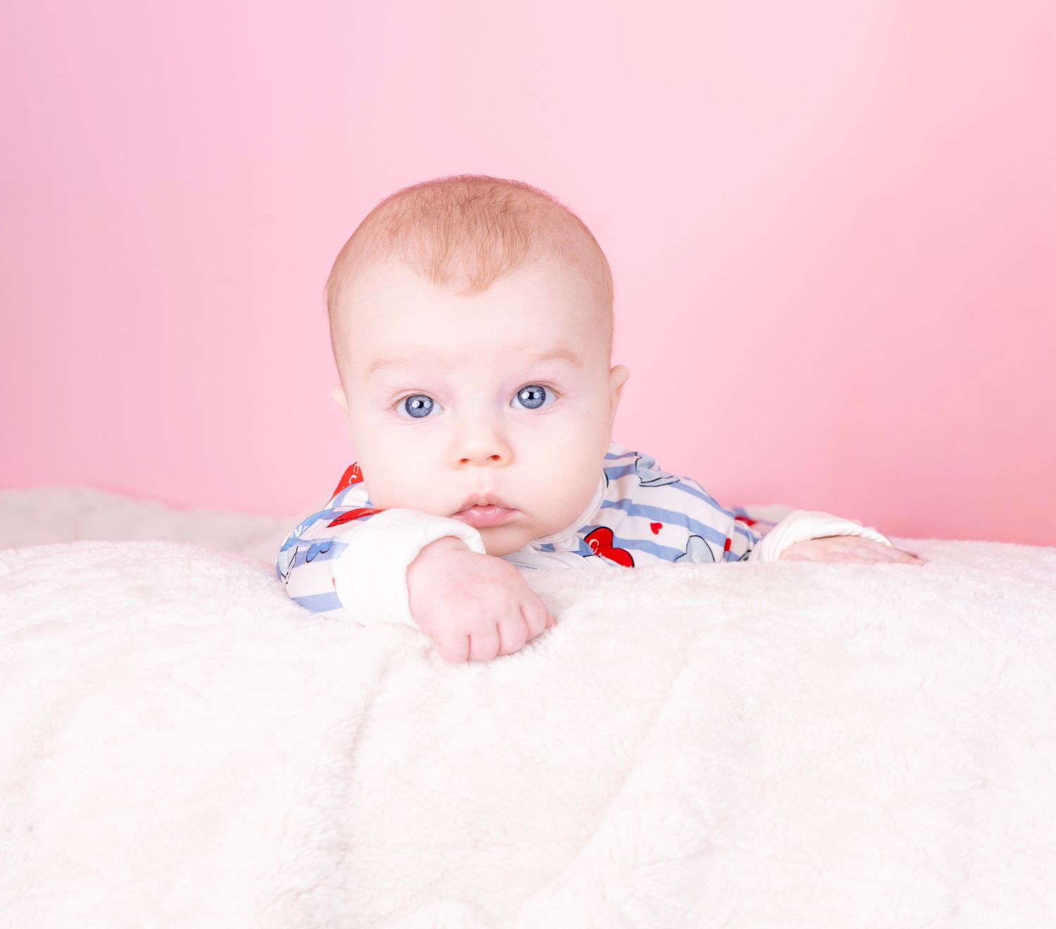 Baby peeks over white blanket against soft pink background.