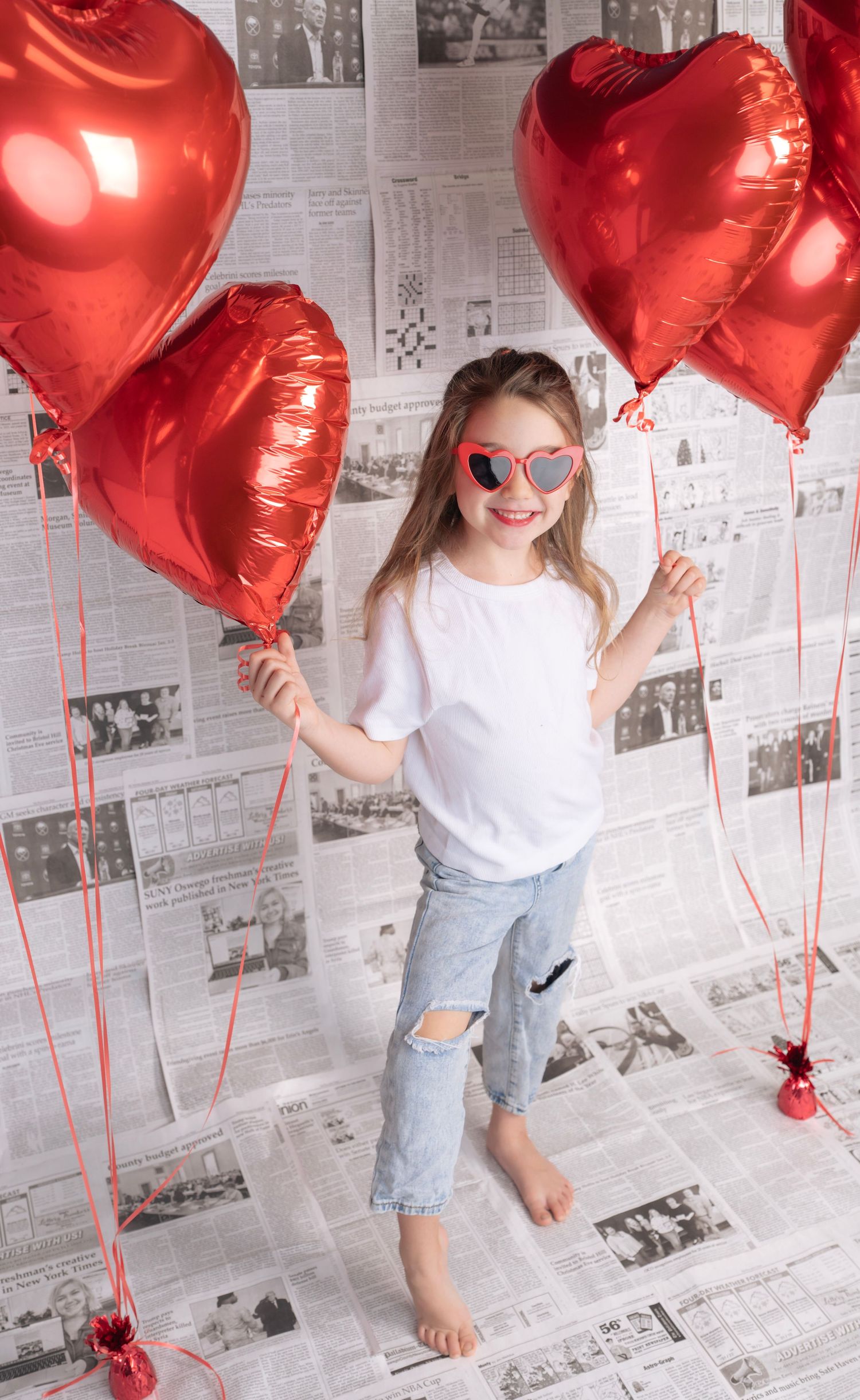 Dancing with red heart balloons against newspaper wall in Valentine's themed shoot.
