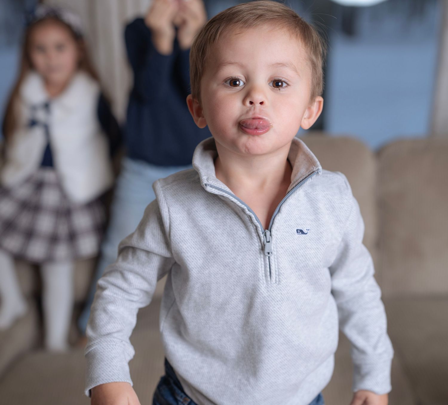 Young children in casual clothing pose together on a light colored couch.