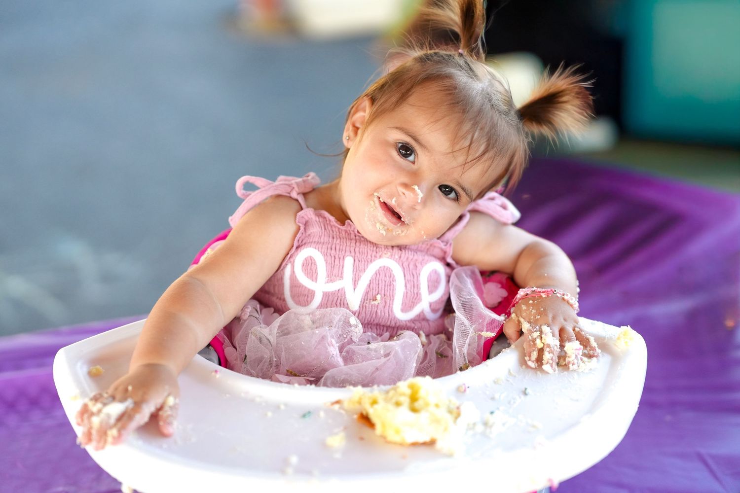Child reaching for cake during first birthday photoshoot with purple backdrop.