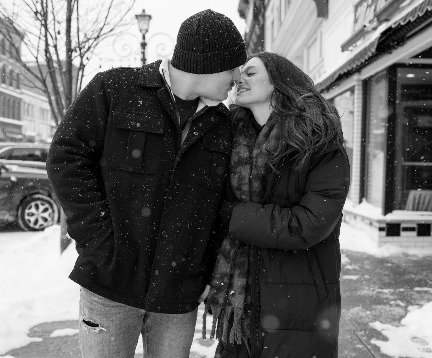 A romantic winter scene of a couple sharing an intimate moment in the snow on a city street.