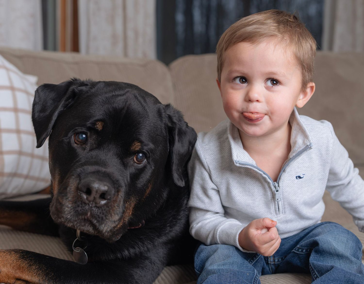 A black Rottweiler dog rests on a couch with children in casual clothing.