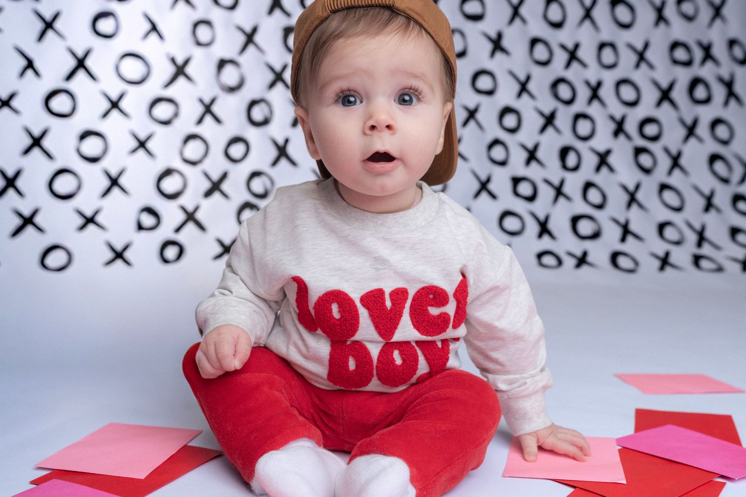 Baby wearing red and white outfit against background with X and O pattern.