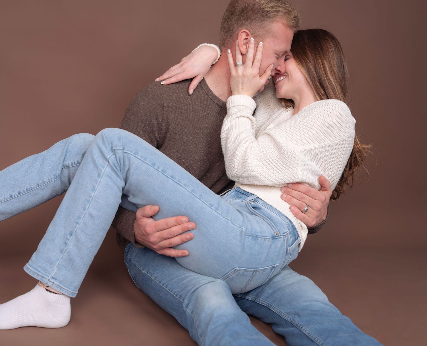 Couple in casual wear lying down and sharing playful moments on brown background.