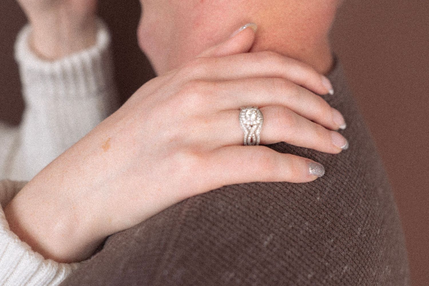 Close-up of a hand wearing an engagement ring resting on a brown sweater.