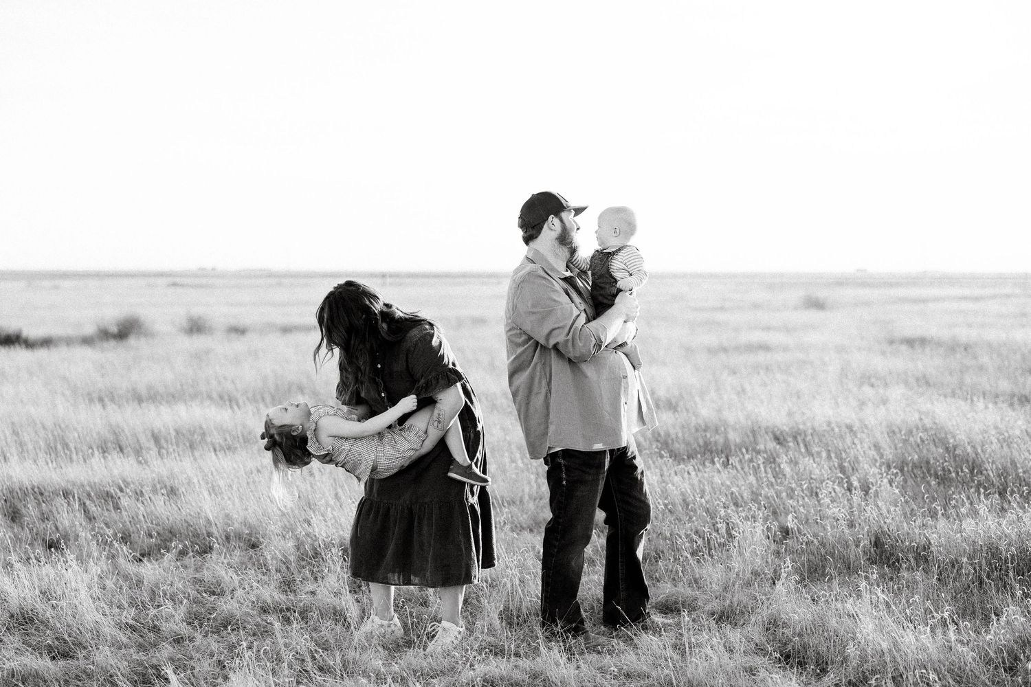 Romantic couple embracing in a scenic field during sunset while photographer captures their special moment.