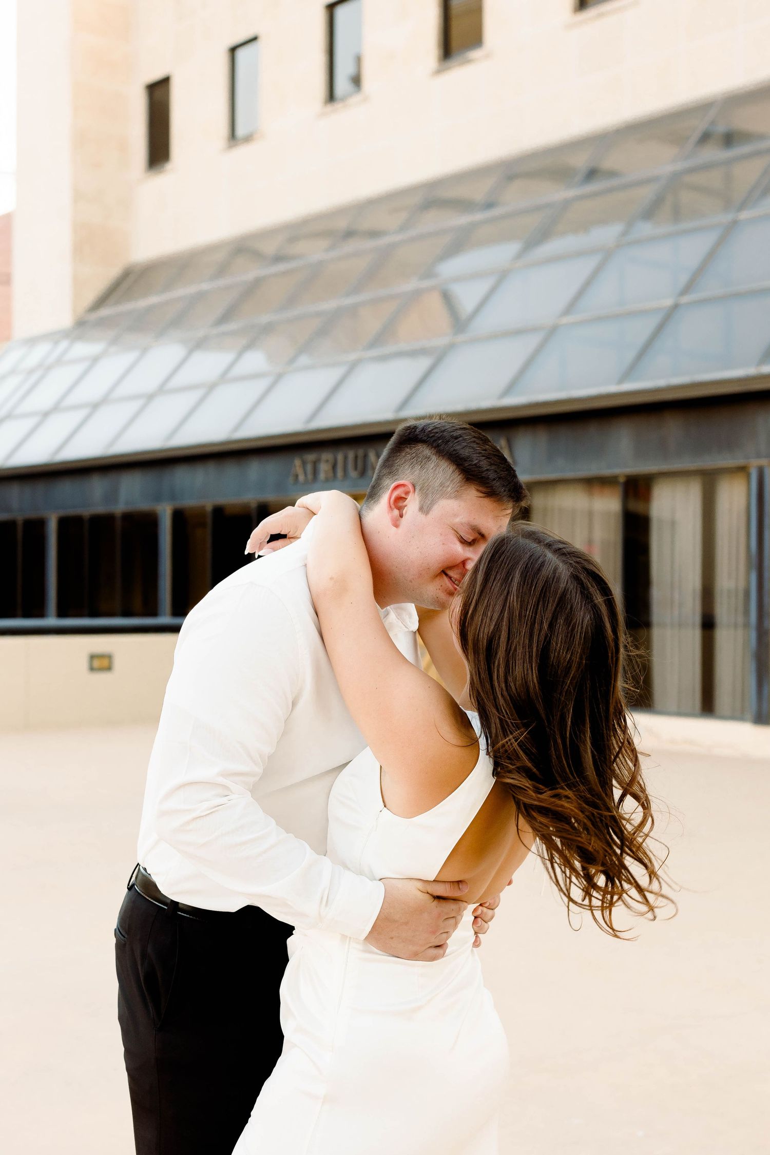 Intimate dance poses captured outside modern building with glass features.
