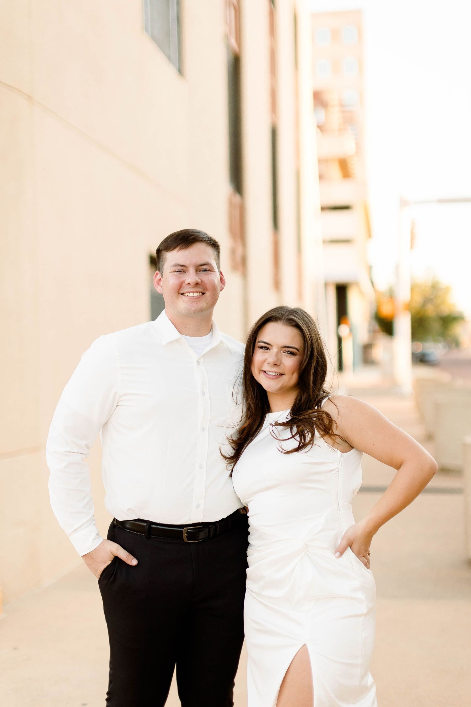 A couple in formal attire shares a joyful moment against a light-colored wall.