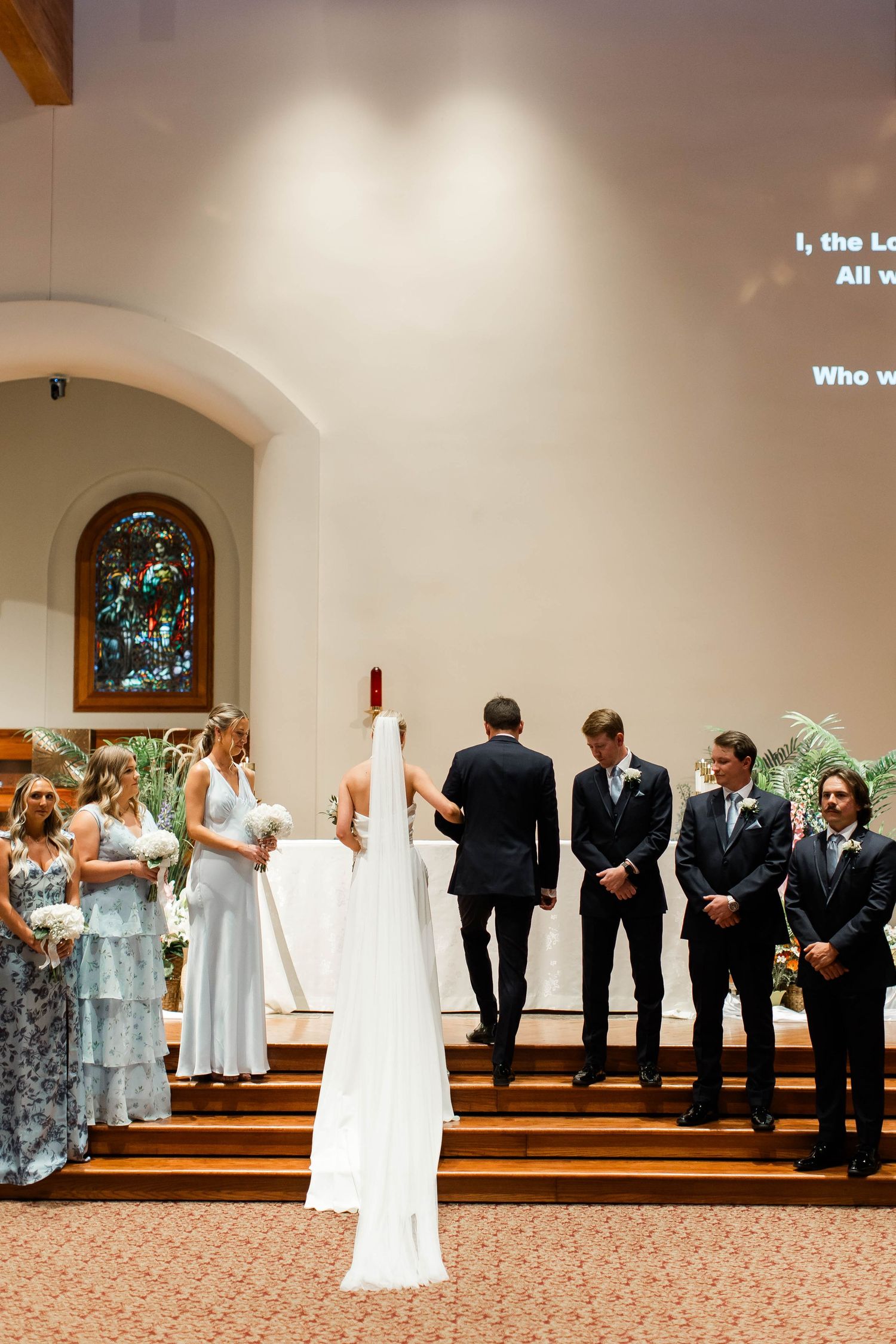 Wedding party lined up in church sanctuary with bridesmaids in light blue dresses and groomsmen in dark suits.