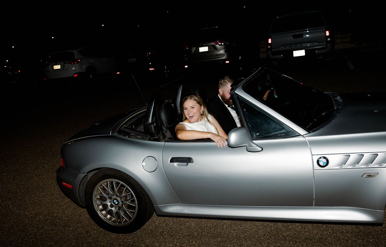 Silver BMW sports car parked at night with decorative lighting in the background.