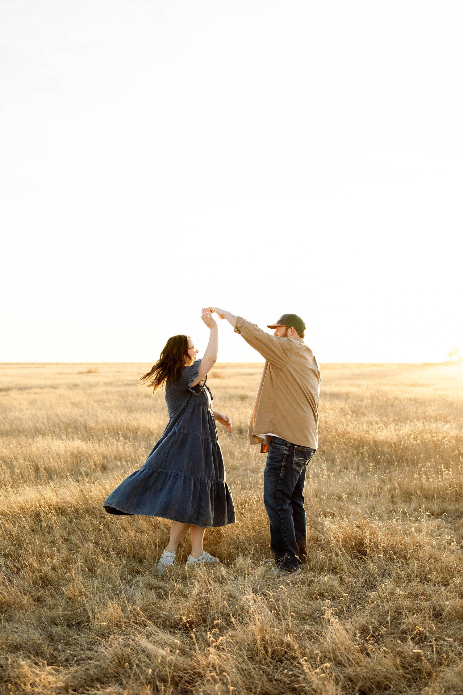A couple dances together in a golden wheat field at sunset creating a romantic silhouette against the warm sky.
