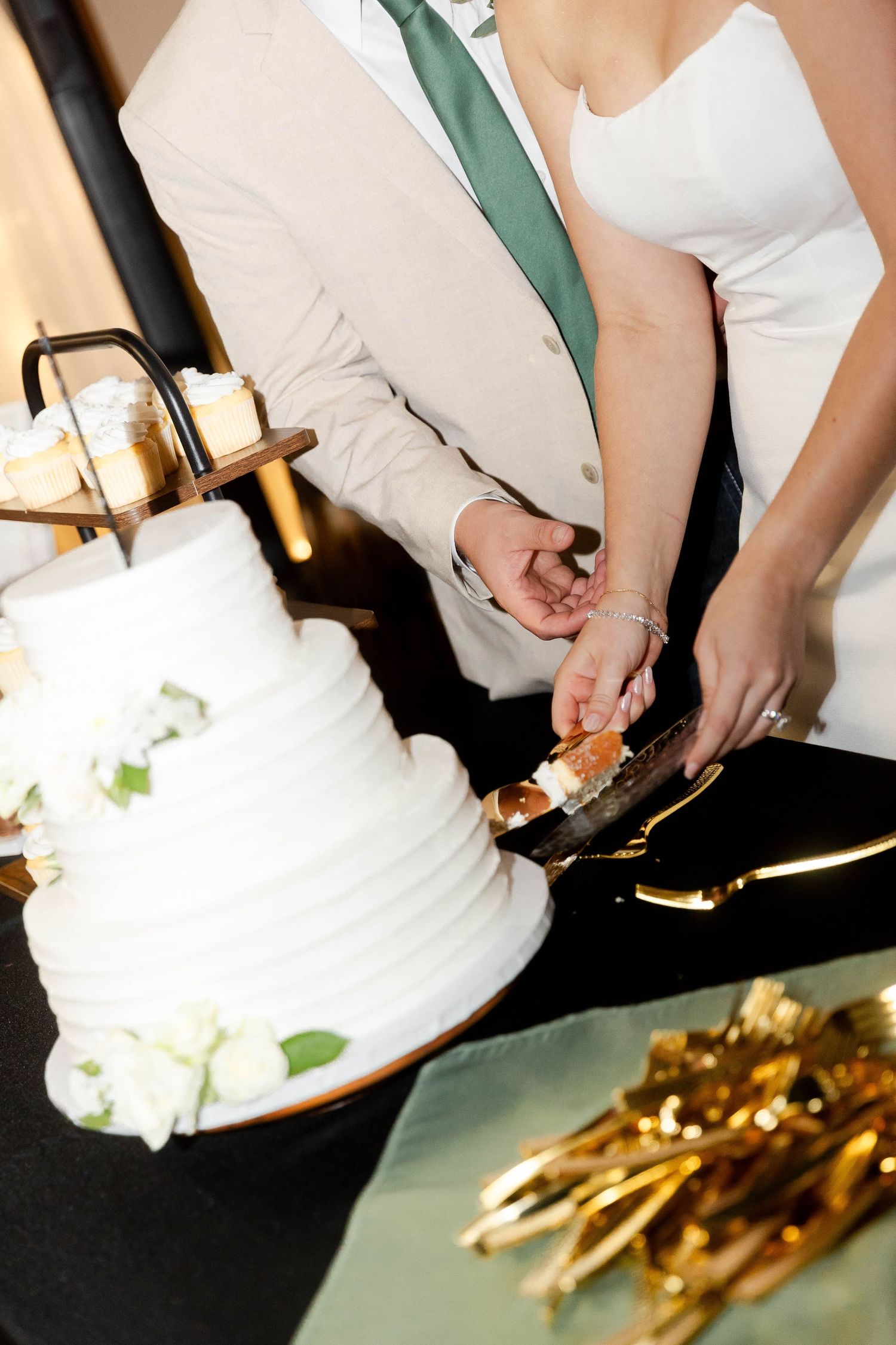 Close-up of wedding cake cutting ceremony with elegant white dress and gold details visible.