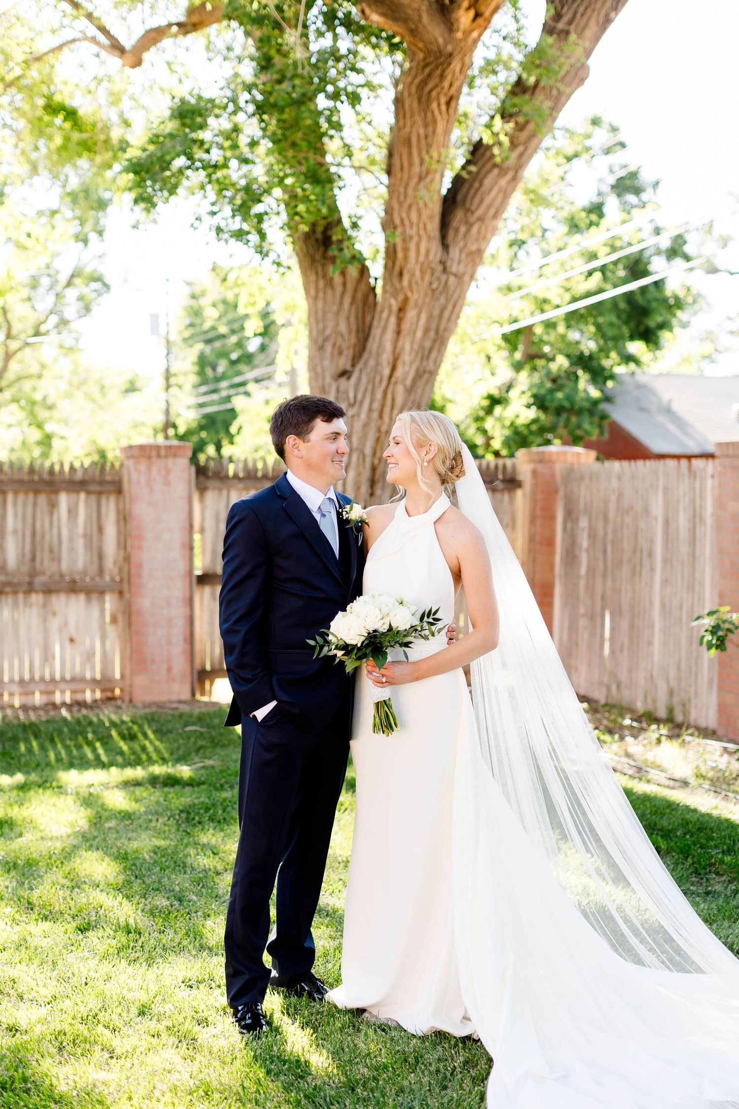 Wedding couple embracing in a backyard garden setting with flowing white veil.