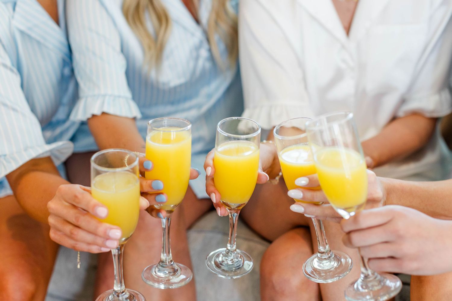 Row of hands holding mimosa glasses in celebration.