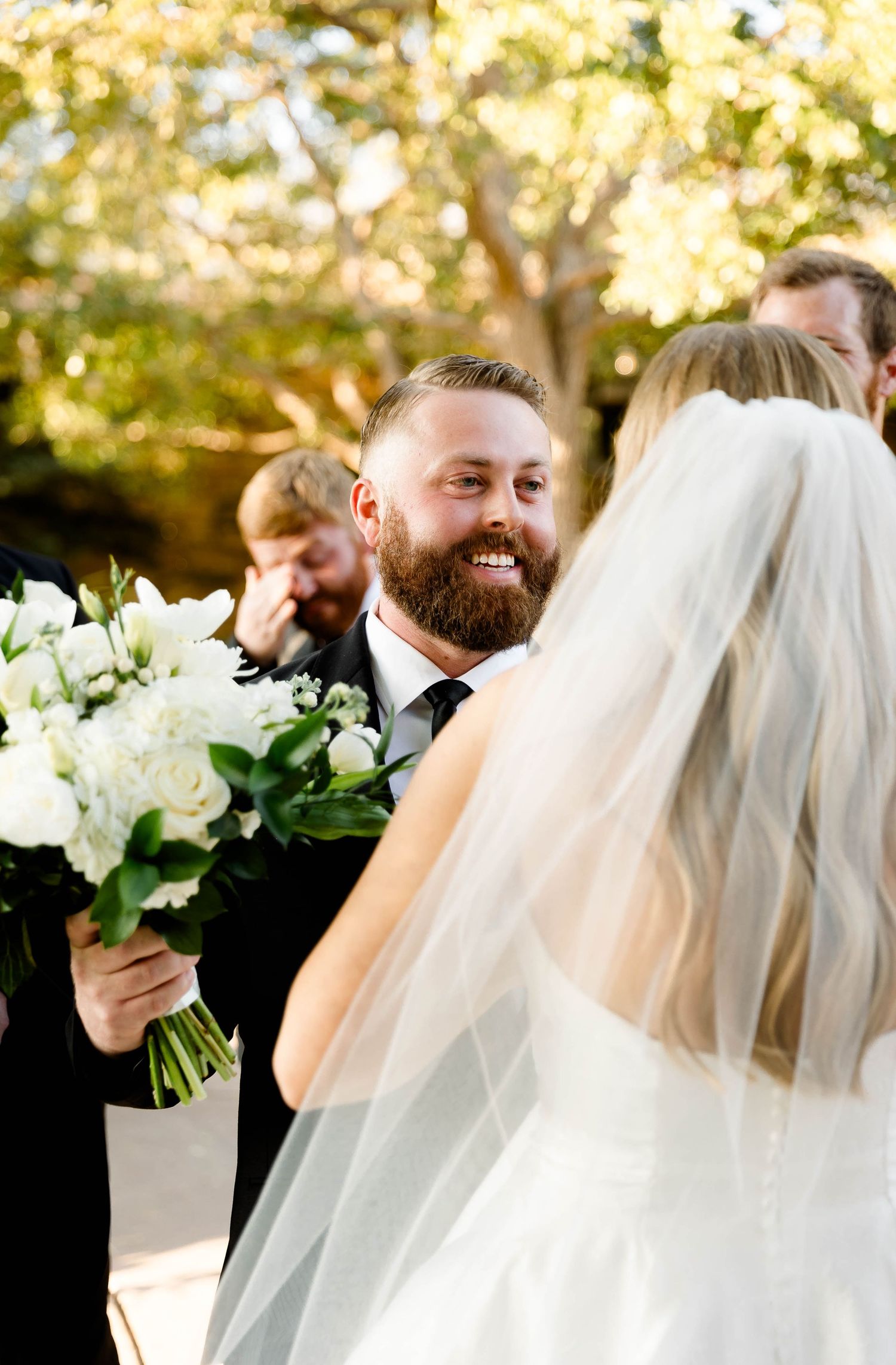 Wedding celebration with elegant white rose bouquets and flowing veils in golden sunlight.