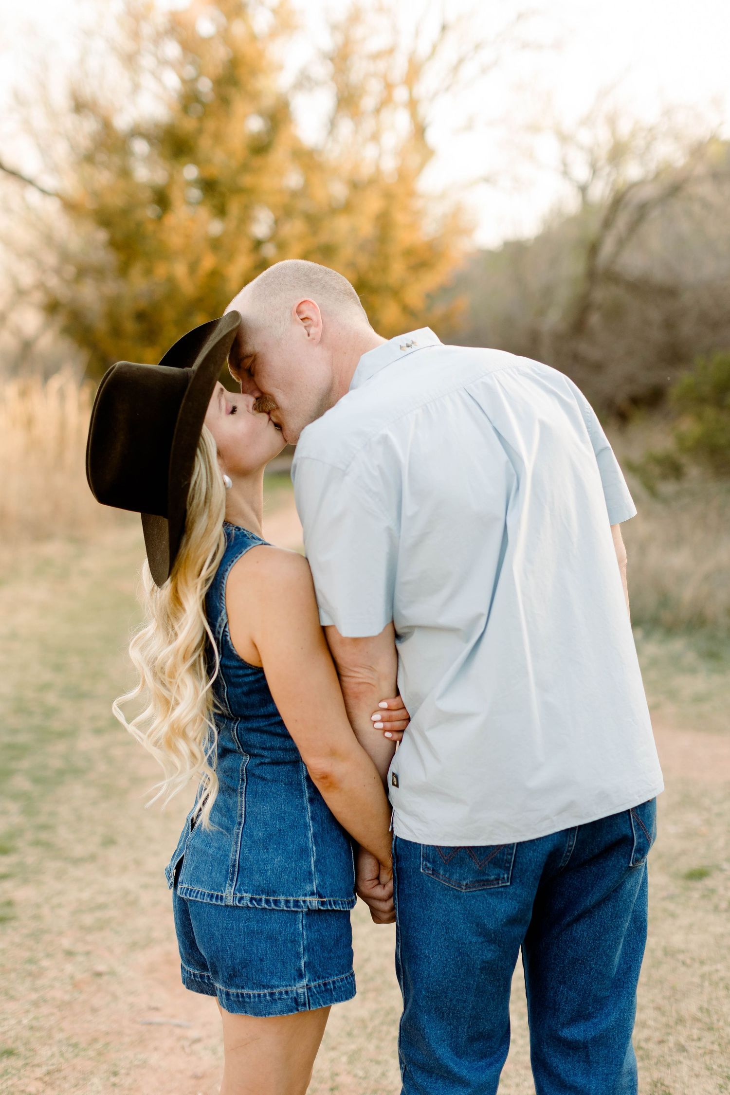 Intimate couple in western wear share tender moments during outdoor photoshoot.