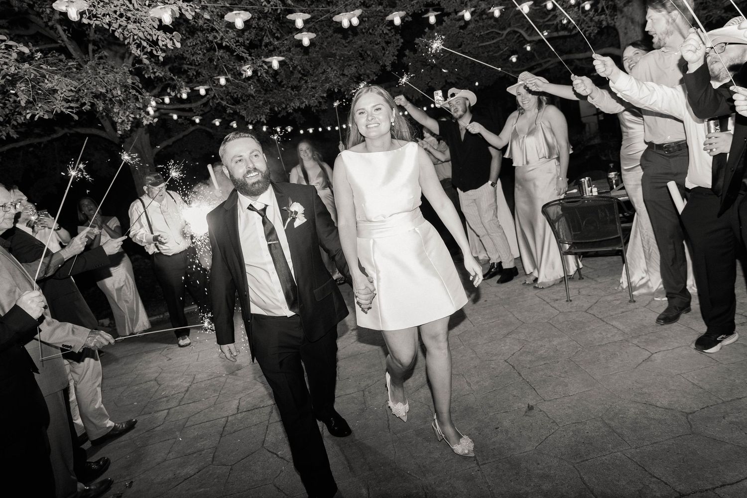 Wedding guests dancing under string lights at an outdoor evening celebration.