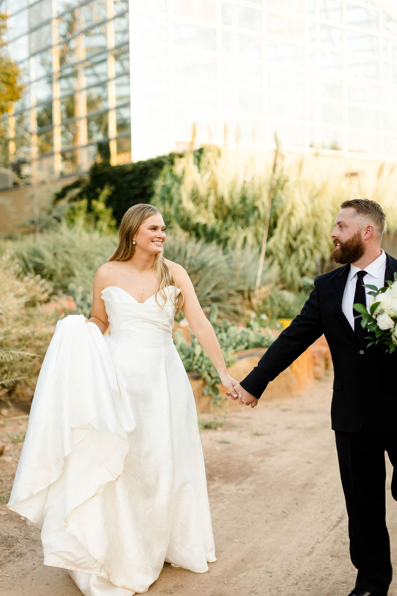Joyful wedding couple dances and twirls on a desert garden path.