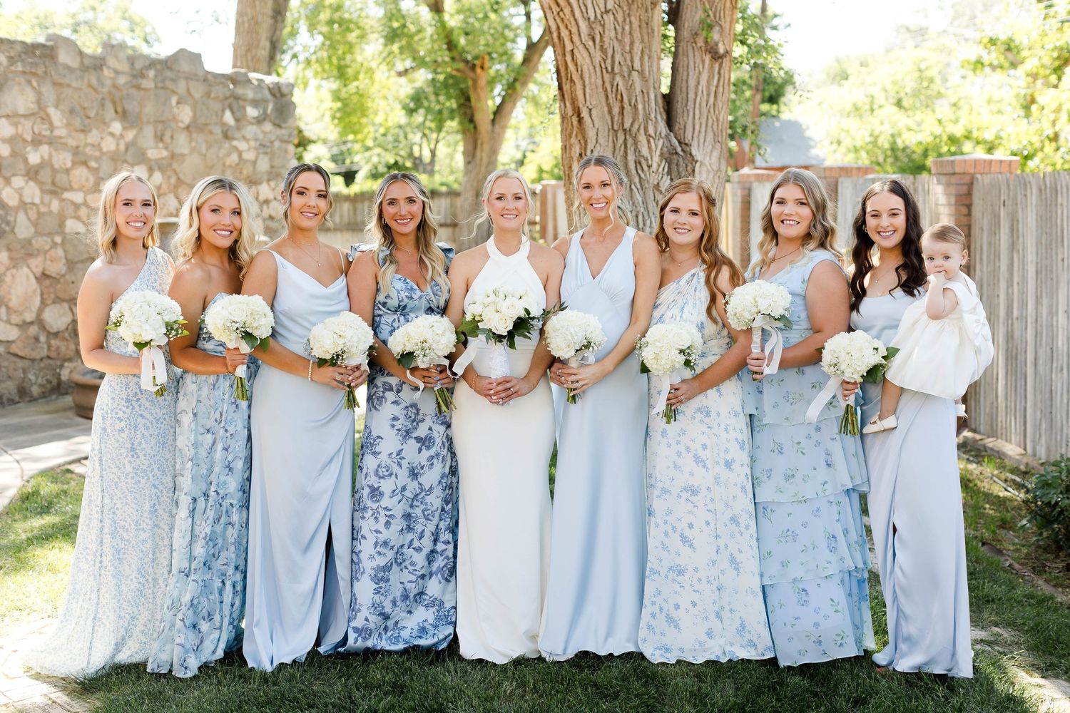 Wedding party in light blue and white dresses standing together outdoors.