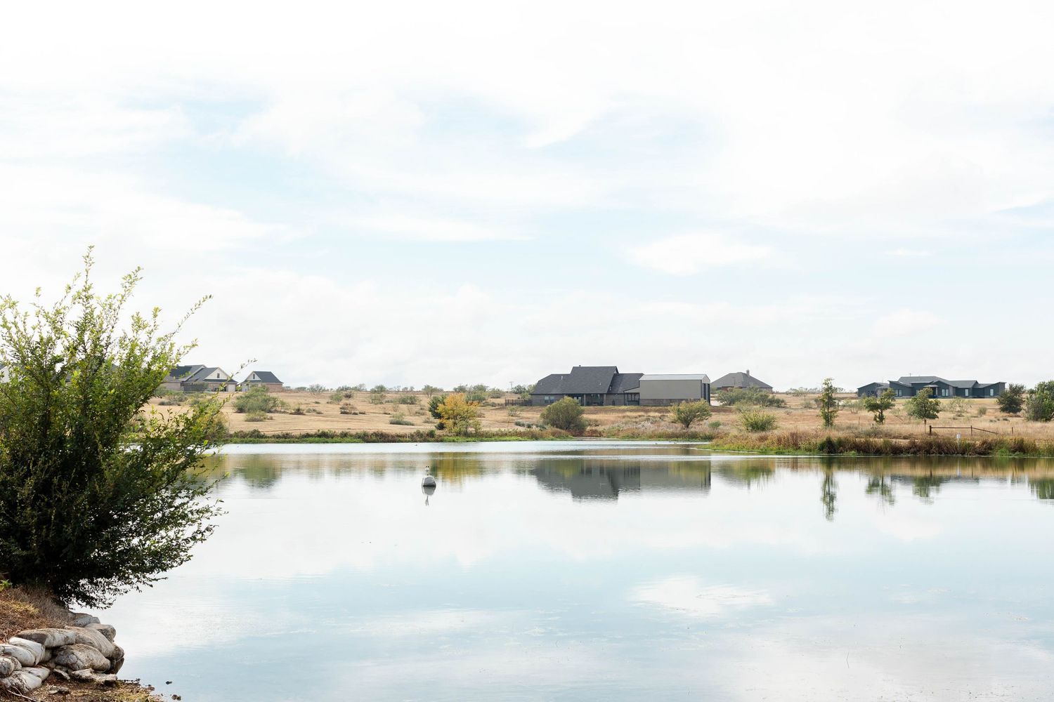 A serene panoramic view of a calm lake with boats and trees reflecting in the still water under a soft sky.