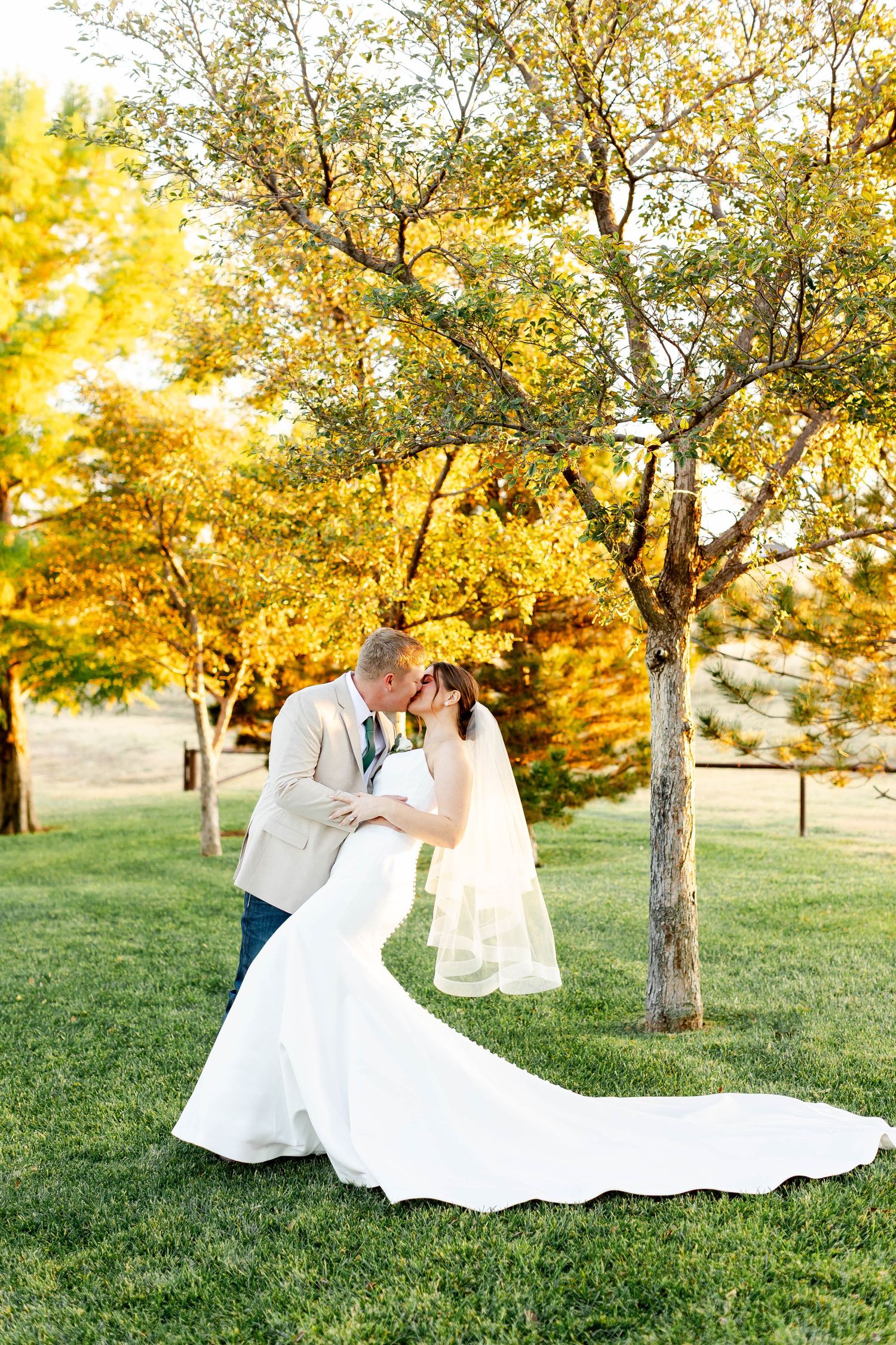 A romantic outdoor wedding photoshoot in a park with golden autumn trees and sunlight filtering through the leaves.