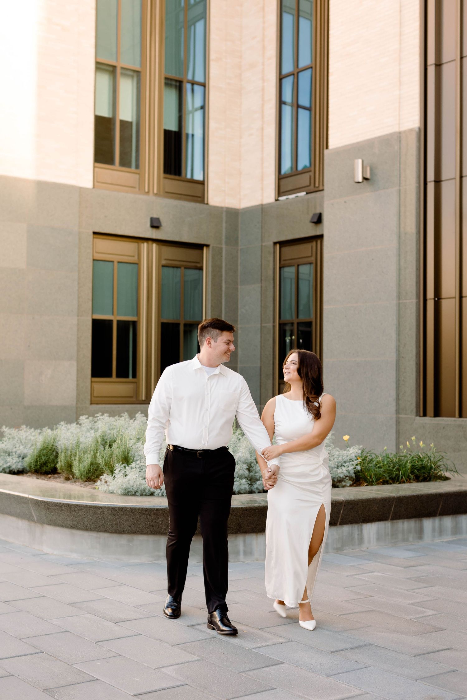 Couple in white and black formal wear walking together on stone patio.