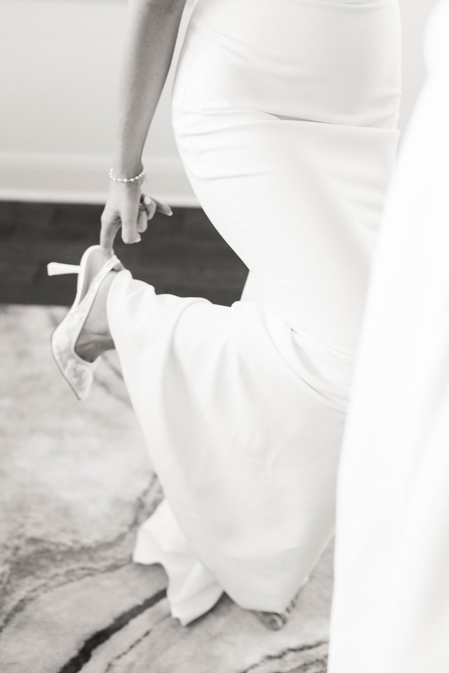 Detail shot of white wedding shoes and dress hem on textured floor.
