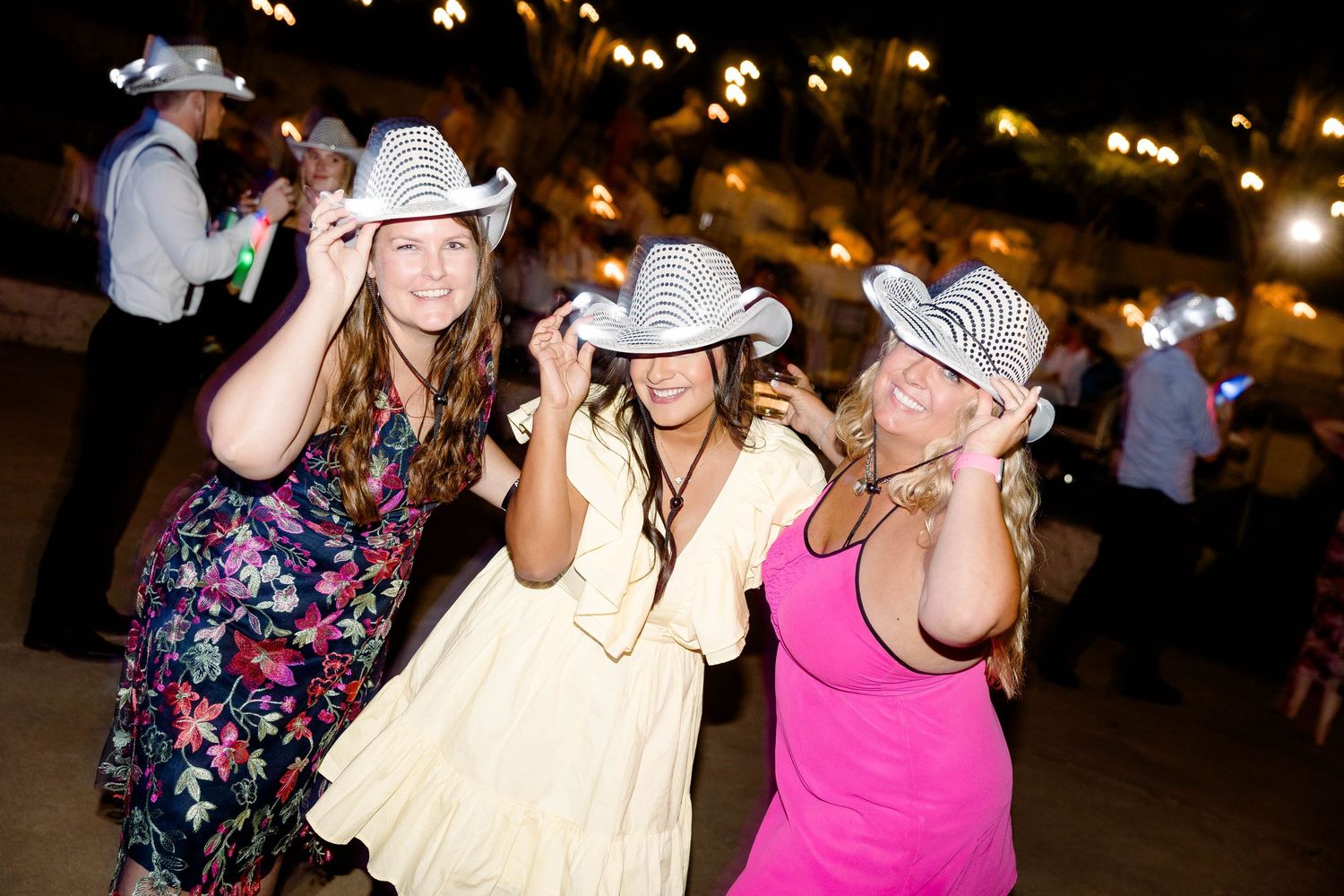 Wedding guests dance and celebrate on a festively lit outdoor dance floor at night.