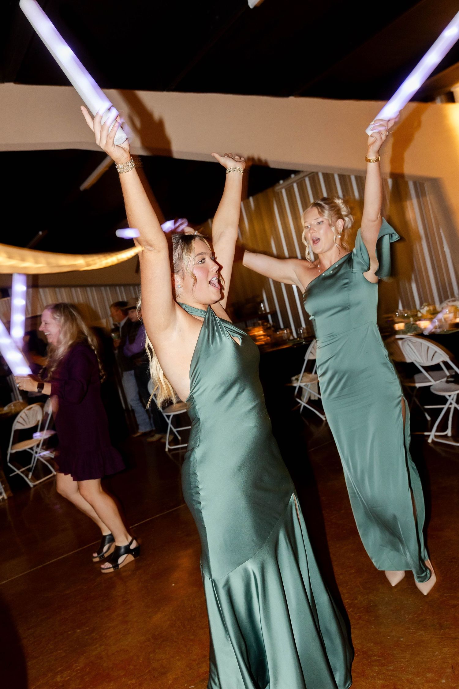 Wedding reception dance floor with guests dancing under purple lighting in green dresses.