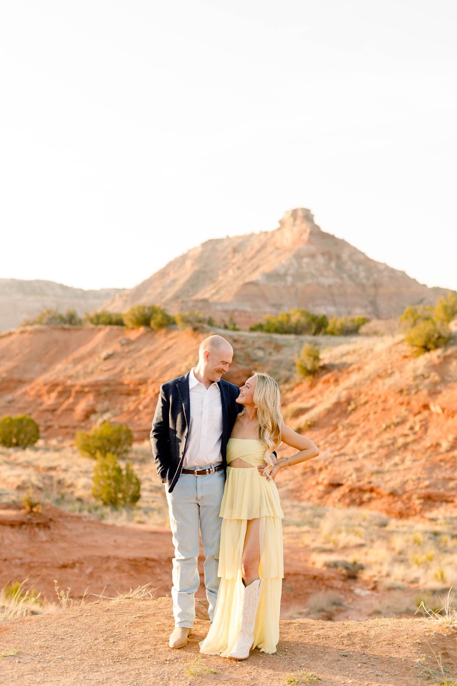 Romantic desert photoshoot with couple in formal wear against red rock formations.