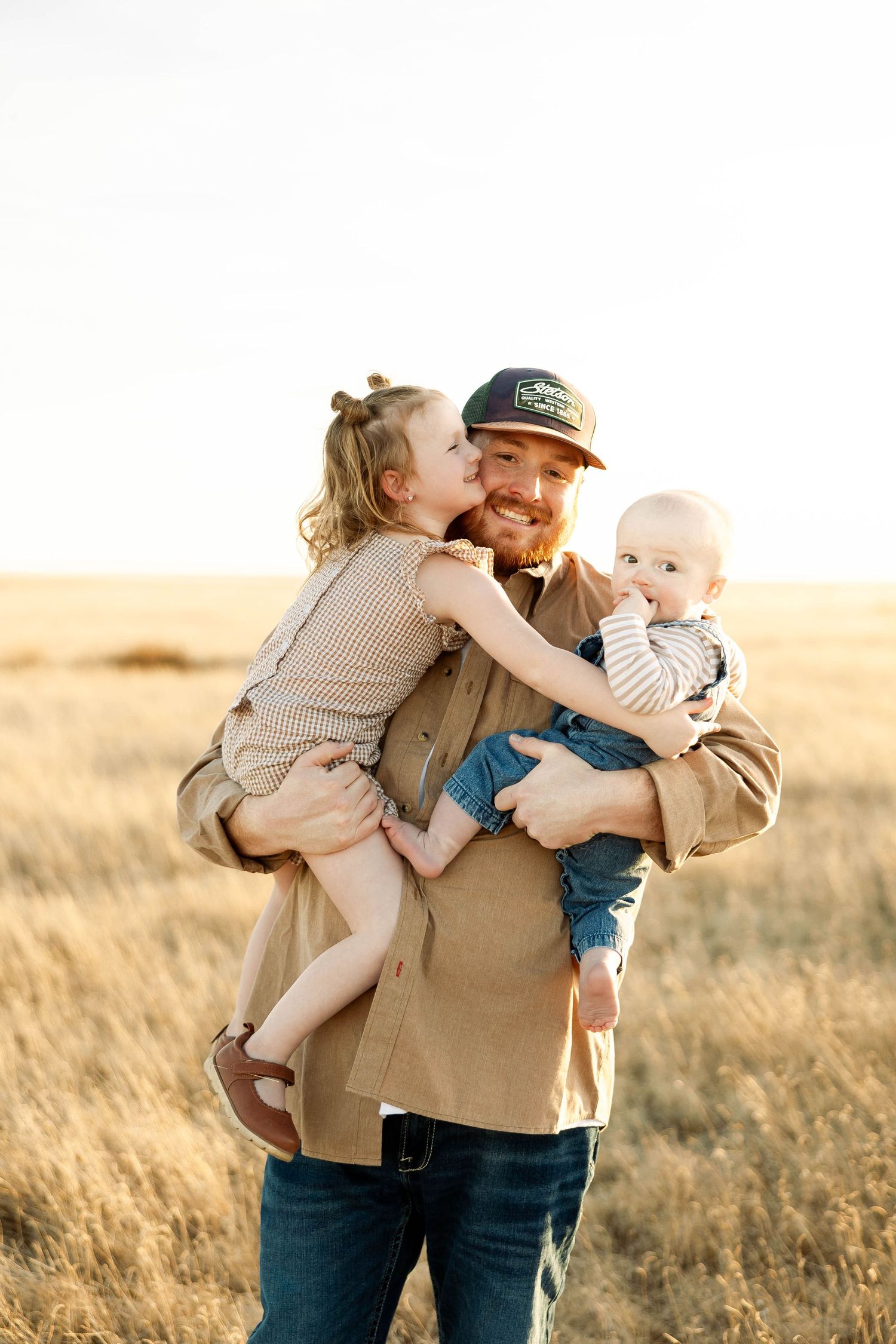 A family shares joyful embraces together in a golden sunlit field at sunset.