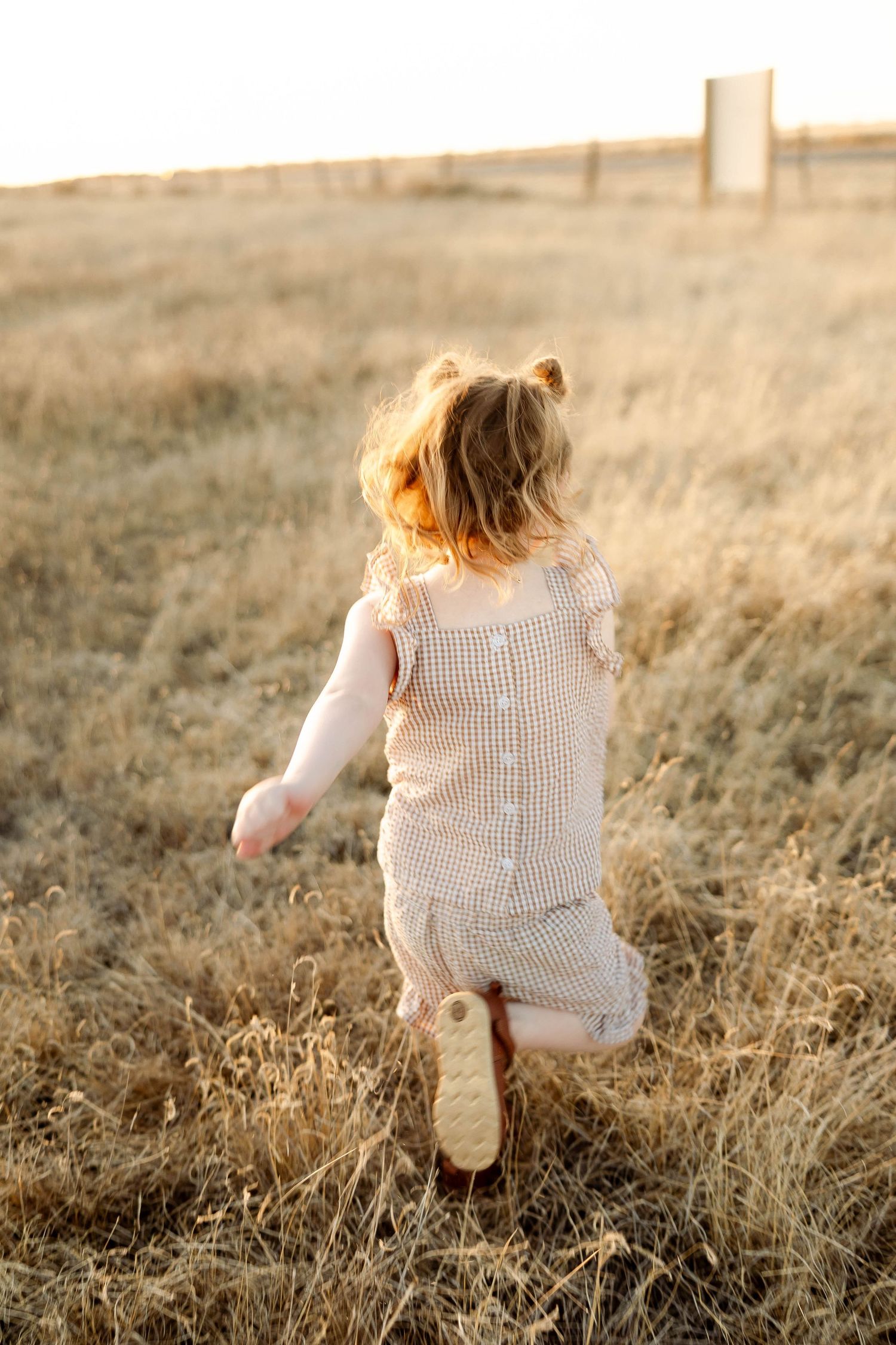Child in a knit sweater dress runs through a golden field at sunset creating a dreamy autumn scene.