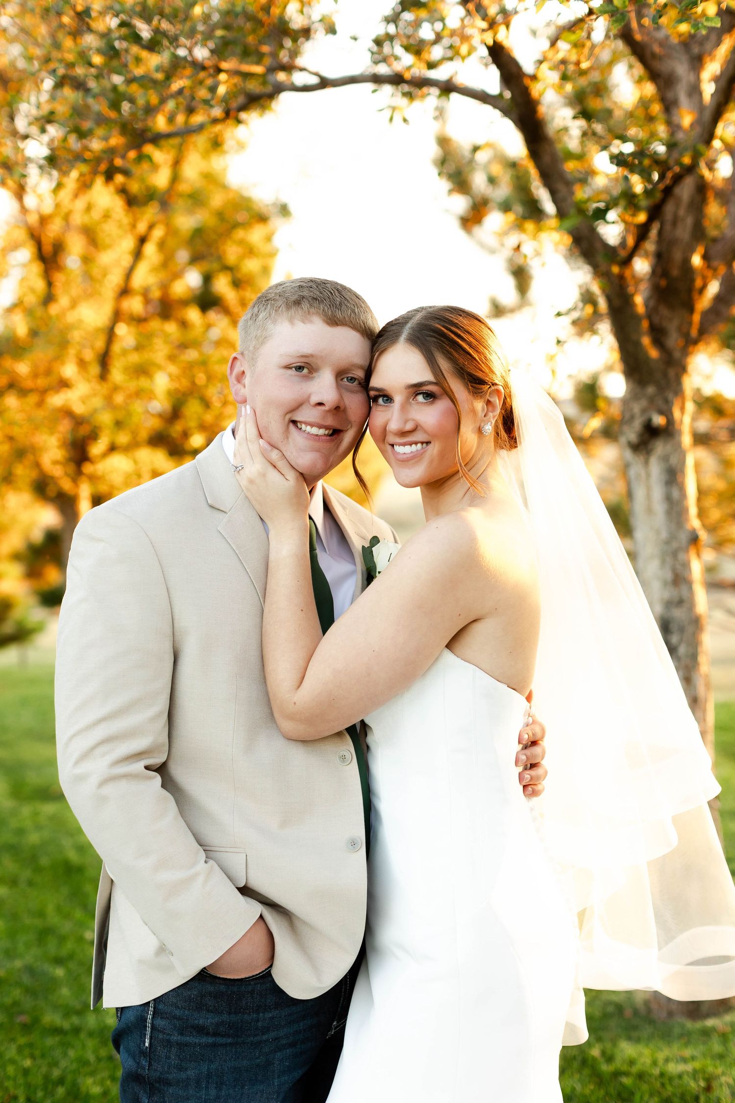 Newlyweds share intimate moments against a backdrop of autumn trees at sunset.