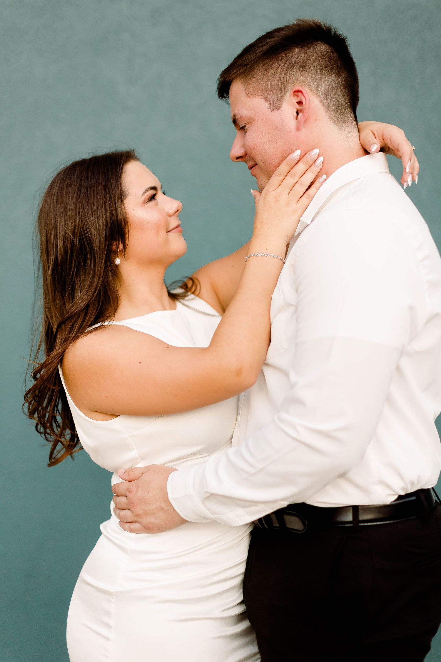 A romantic couple embraces in matching white tops against a teal background.