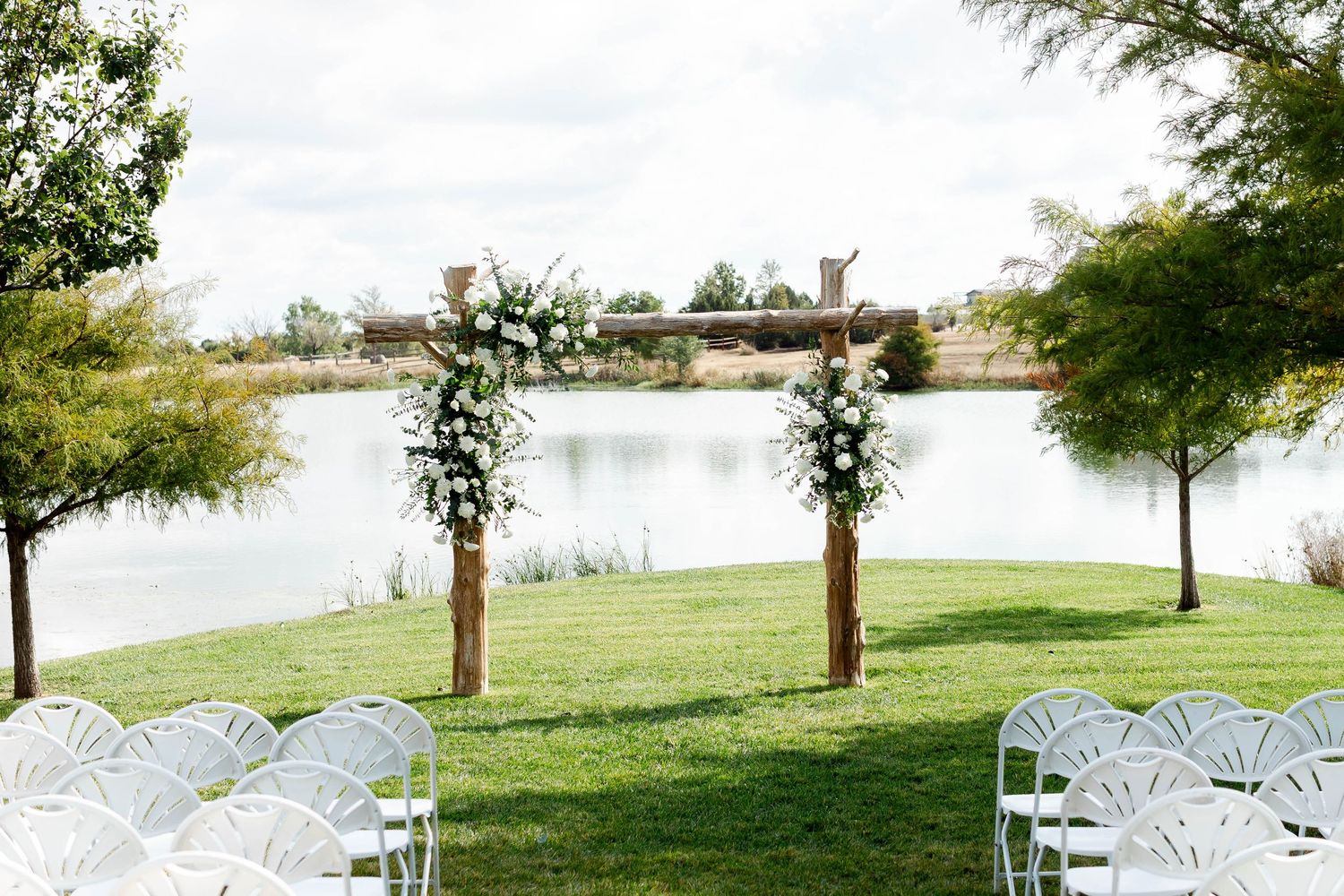 White chairs arranged in rows on a grassy lawn overlooking a lake for an outdoor wedding ceremony.
