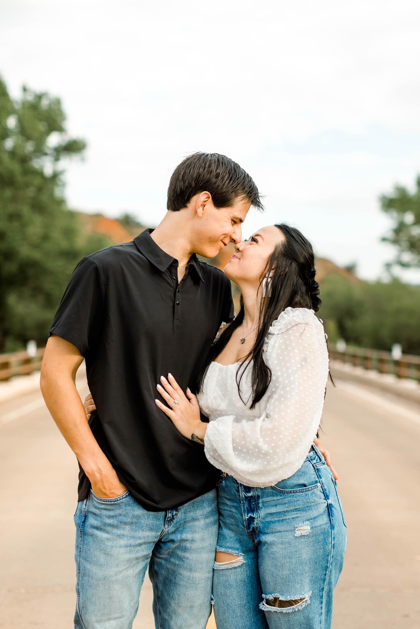 A romantic couple in casual attire sharing tender kisses and embraces on a wooden bridge during a photo session.
