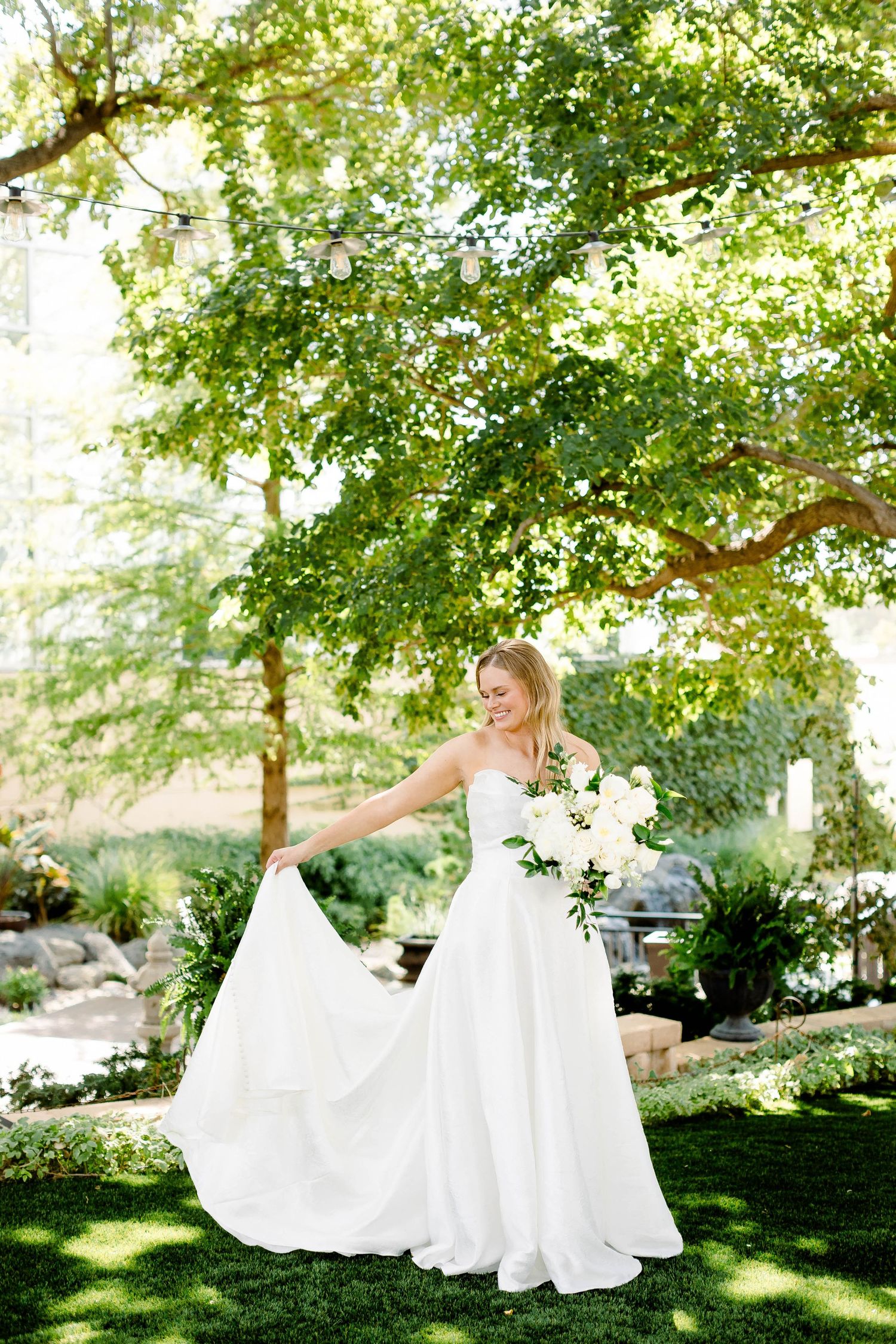 Flowing white wedding dress captured in motion across a sunlit garden landscape.