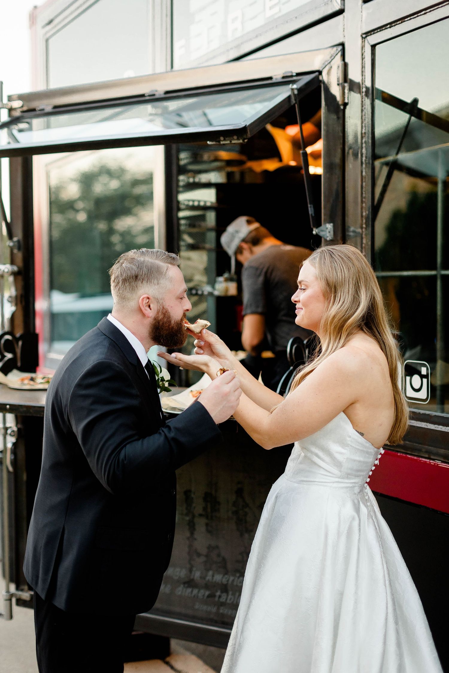 Couple playfully interacts near black food truck windows at their wedding reception.