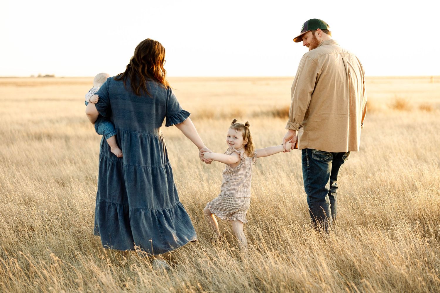 Family walking together through golden wheat field at sunset holding hands and enjoying nature.