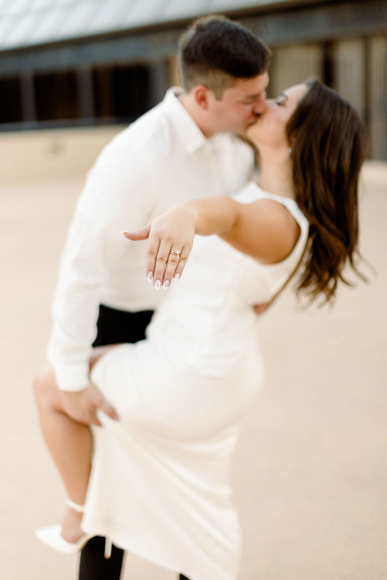 A couple dressed in white and black embrace while sharing a tender moment outdoors.