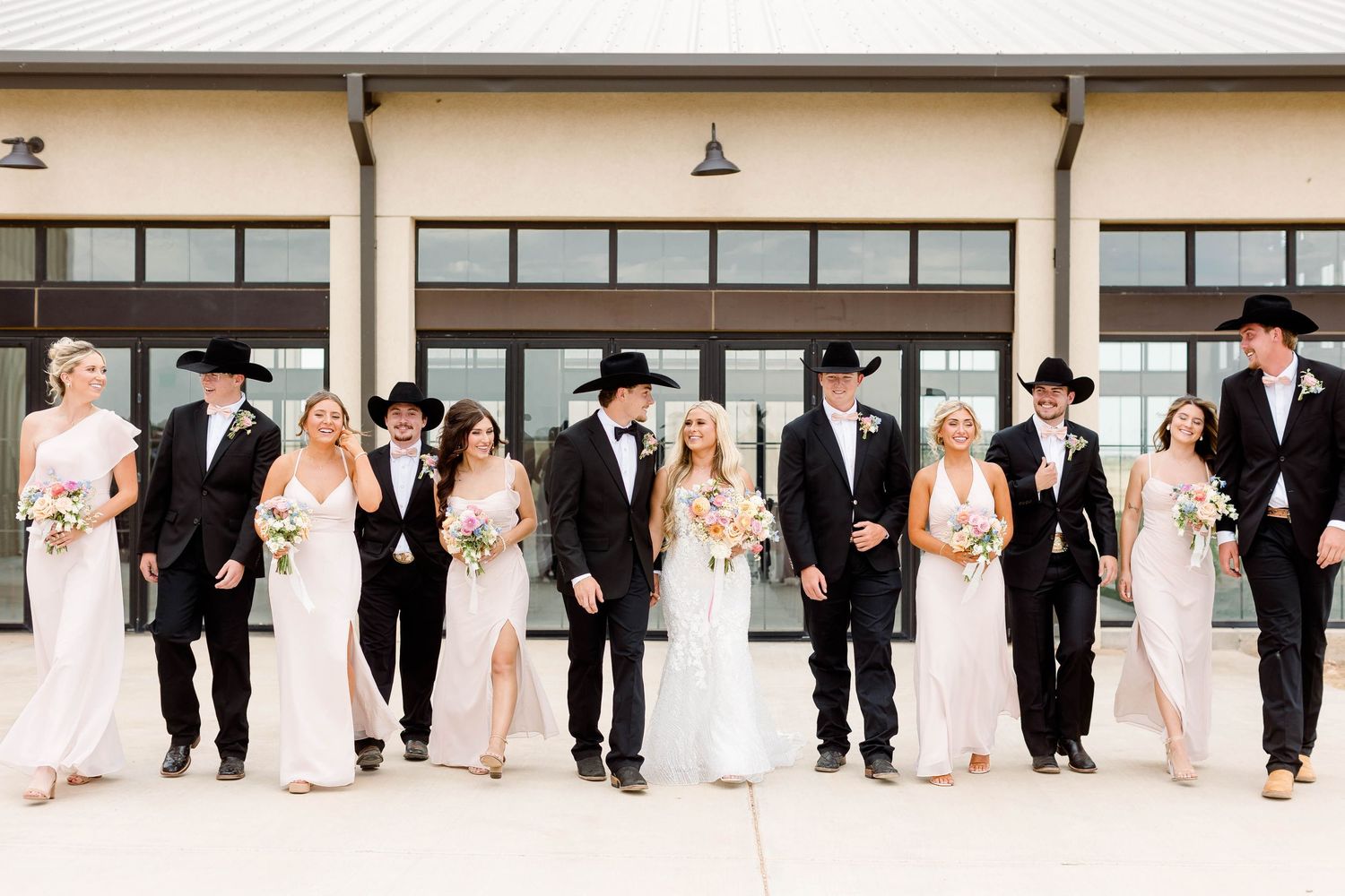 Wedding party lined up against a white wall in formal attire.