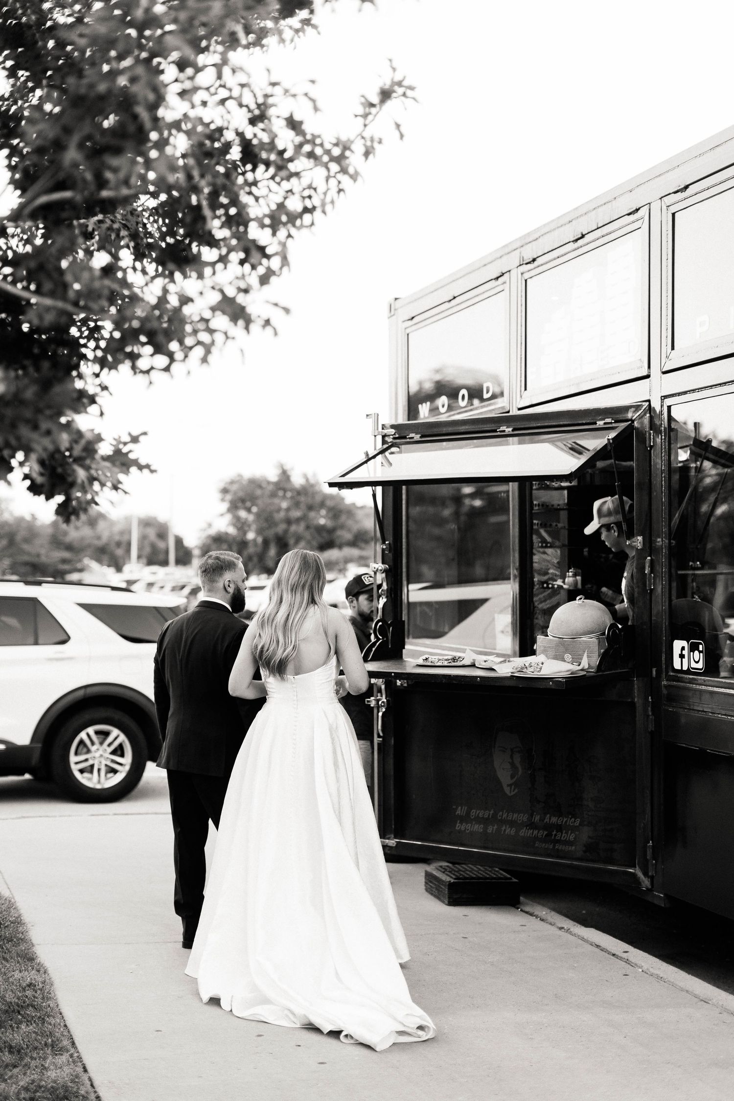 Wedding couple walks toward black food trucks in an outdoor venue.