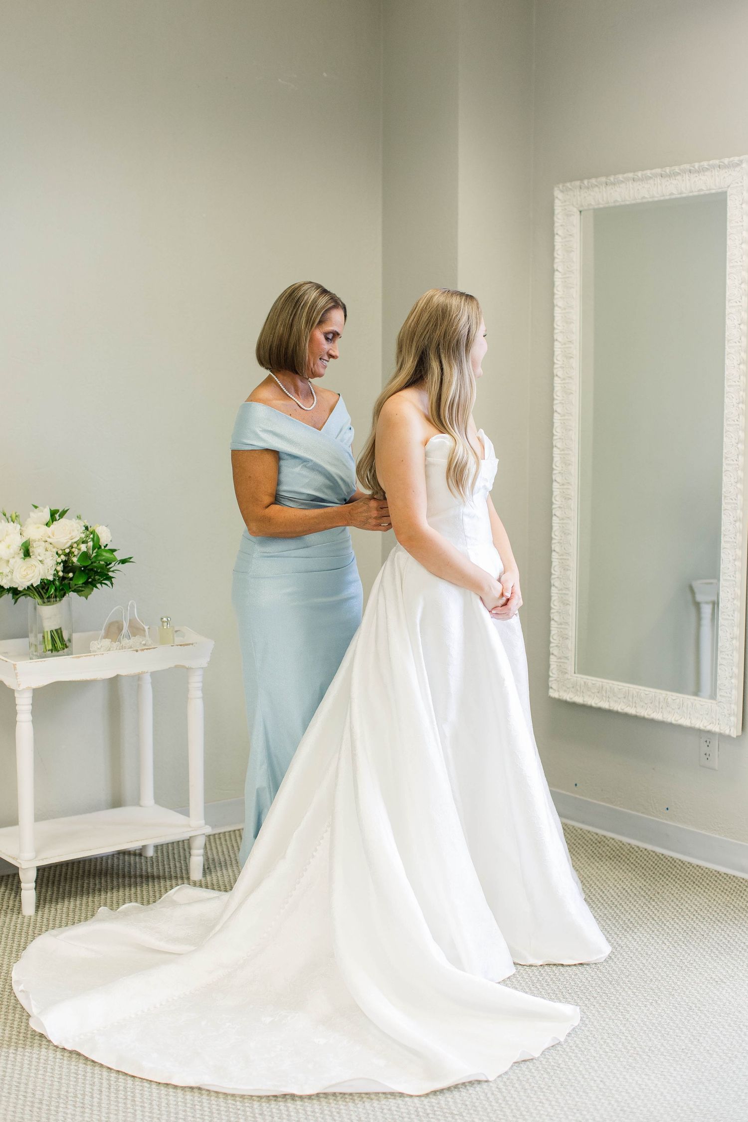 Wedding dress fitting session with flowing white gown in bright room.