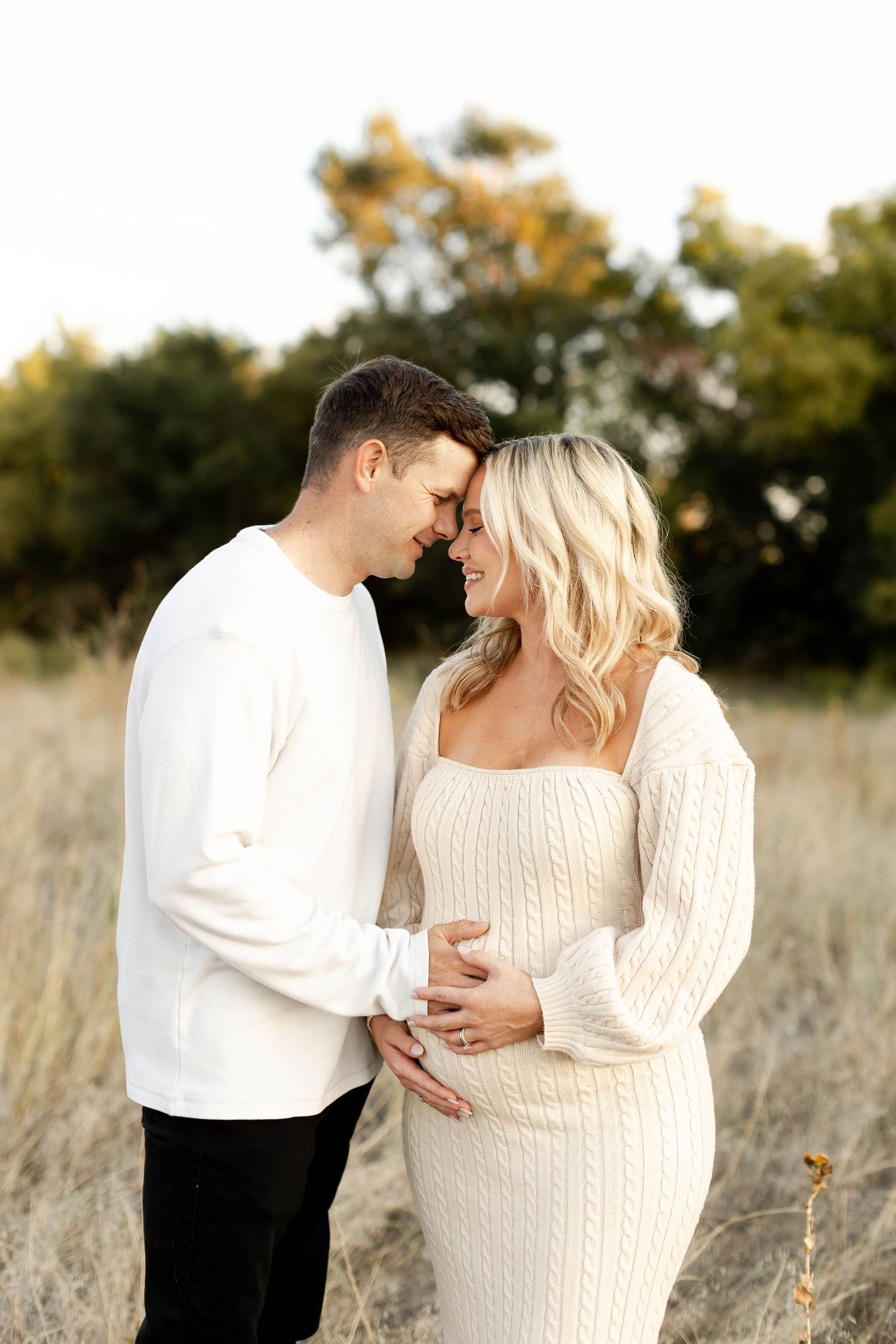 Intimate maternity photos of couple embracing in a sunlit field.